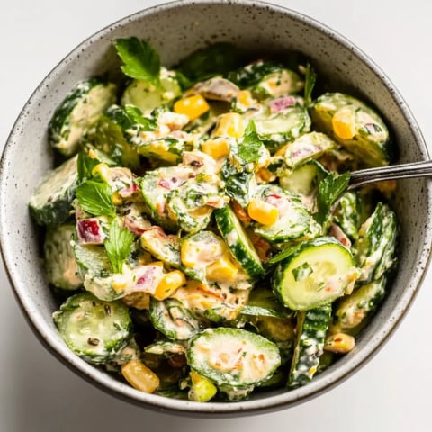 A bowl of fresh cucumbers, corn, and greens for a light salad.